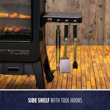 Black metal grill side shelf with three tool hooks, holding tongs, spatula, and brush. Accessible and organized design.