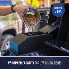 Person pours wood pellets into a grill hopper with a 7 lb capacity, ideal for slow-cooked dishes.