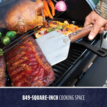 "Large black grill with 849-square-inch cooking space, featuring meats and vegetables."