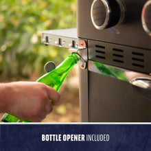 Built-in metal bottle opener on a grill, shown opening a green glass bottle. Easy access for outdoor use.