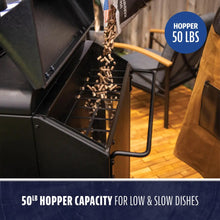 Black pellet grill with open hopper being filled; 50 lb capacity for extended, slow cooking.