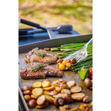 Grilled steak with asparagus, cherry tomatoes, and potatoes on a black tray.