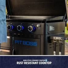 Pit Boss grill with non-stick ceramic coated, rust-resistant cooktop. Features blue-lit knobs and utensil hooks.