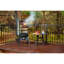 Black vertical electric smoker with multiple racks, emitting smoke, on a wooden deck.