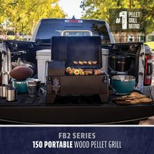 FB2 Series 150 Portable Wood Pellet Grill on a truck tailgate, grilling meat and veggies, with bowls and utensils nearby.