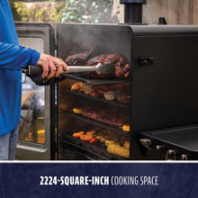 Large black smoker with 2224-square-inch cooking space, multiple racks filled with meats and vegetables, steam visible.