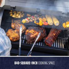 Black grill with 840-square-inch cooking space, cooking meats and vegetables.